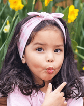 Toddler girl is wearing a pink gingham print top knot headband from By Bella Boutique.